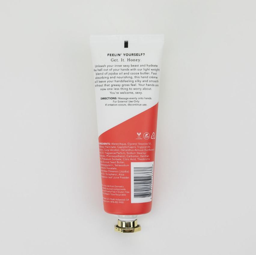The back of a hand cream tube, showing the text and barcode, with a red and white design and a gold cap, photographed on a light gray background.