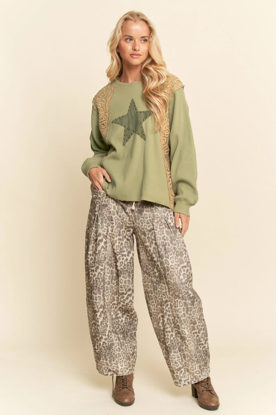 Woman wearing a green sweater with a star design and patterned pants on a beige background