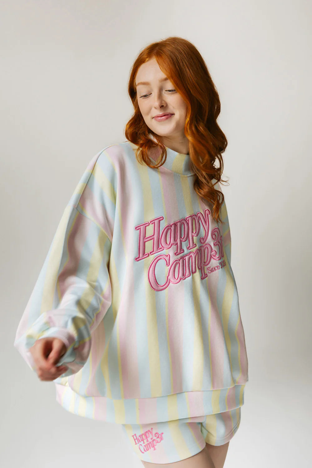 Woman wearing a pastel striped sweater with 'Happy Campers' text on a plain background