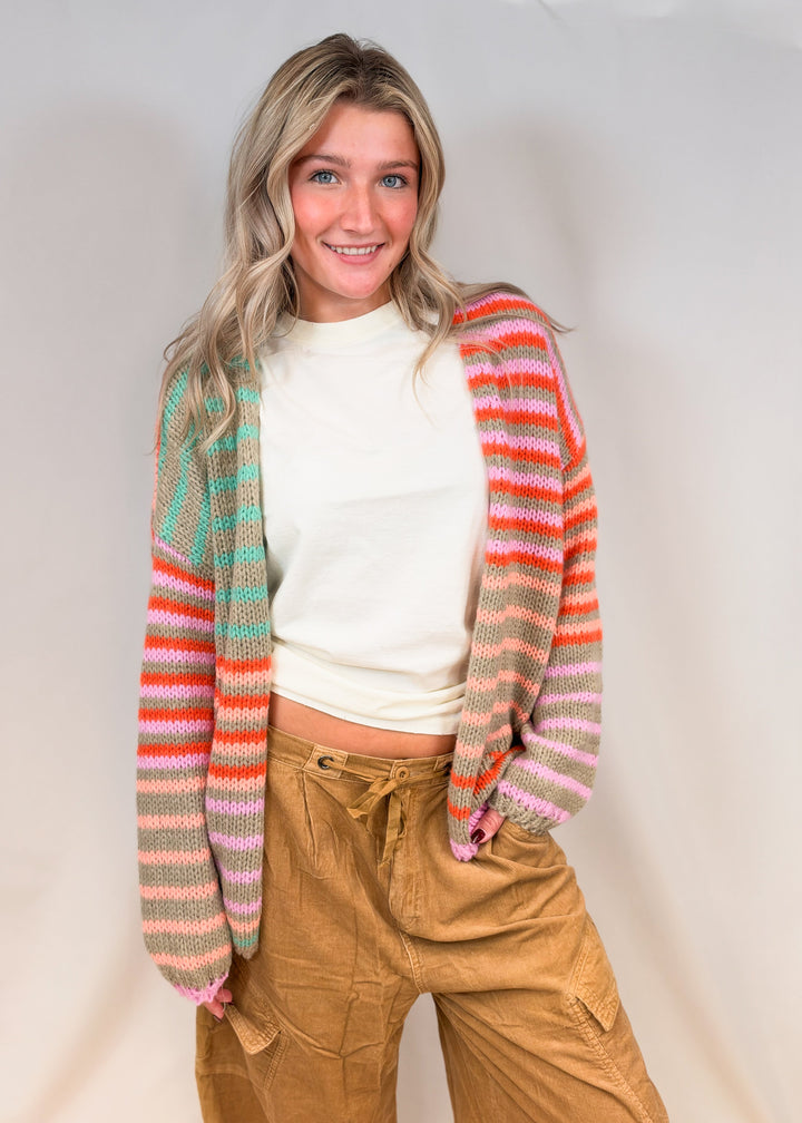 Woman wearing colorful stripe cardigan with cream tee and camel cord pants on plain background