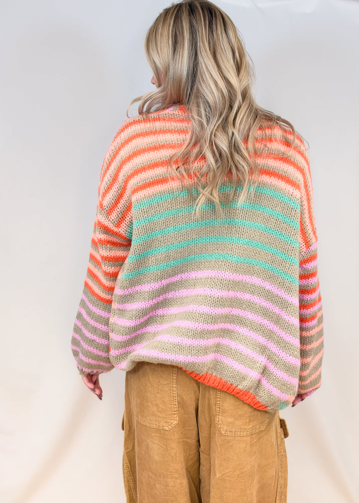 Woman shown from back view wearing colorful stripe cardigan with camel color cord pants on plain background