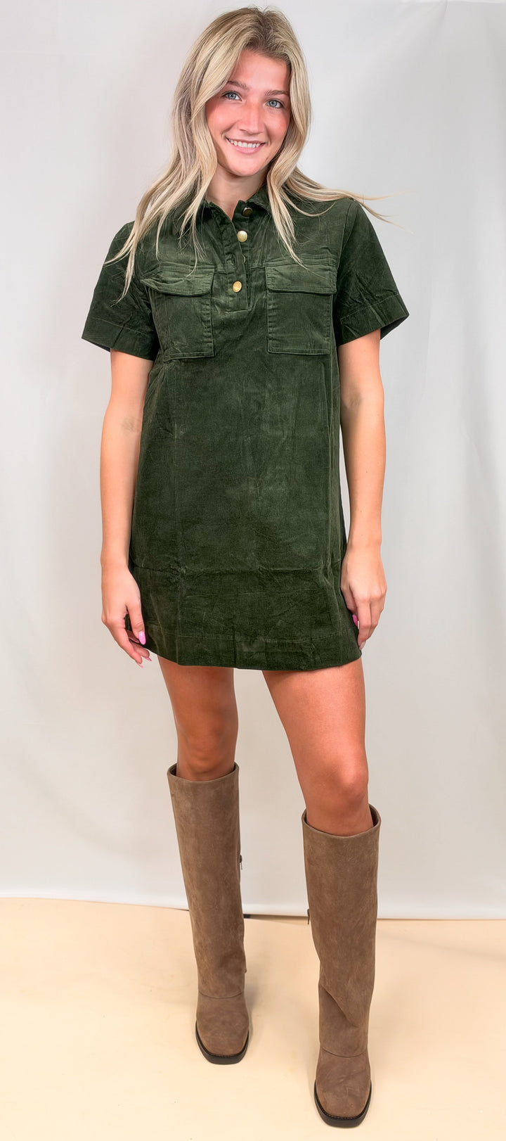 Woman wearing green corduroy dress with knee high boots on plain background