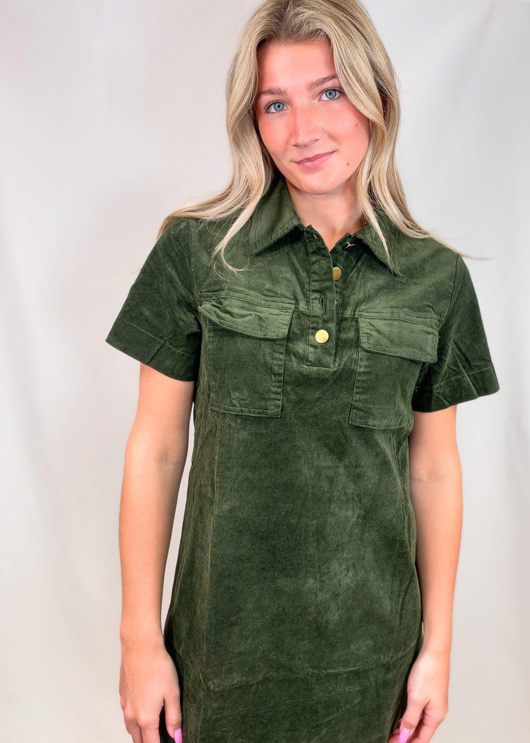 Woman wearing dark green short sleeve corduroy dress on plain background