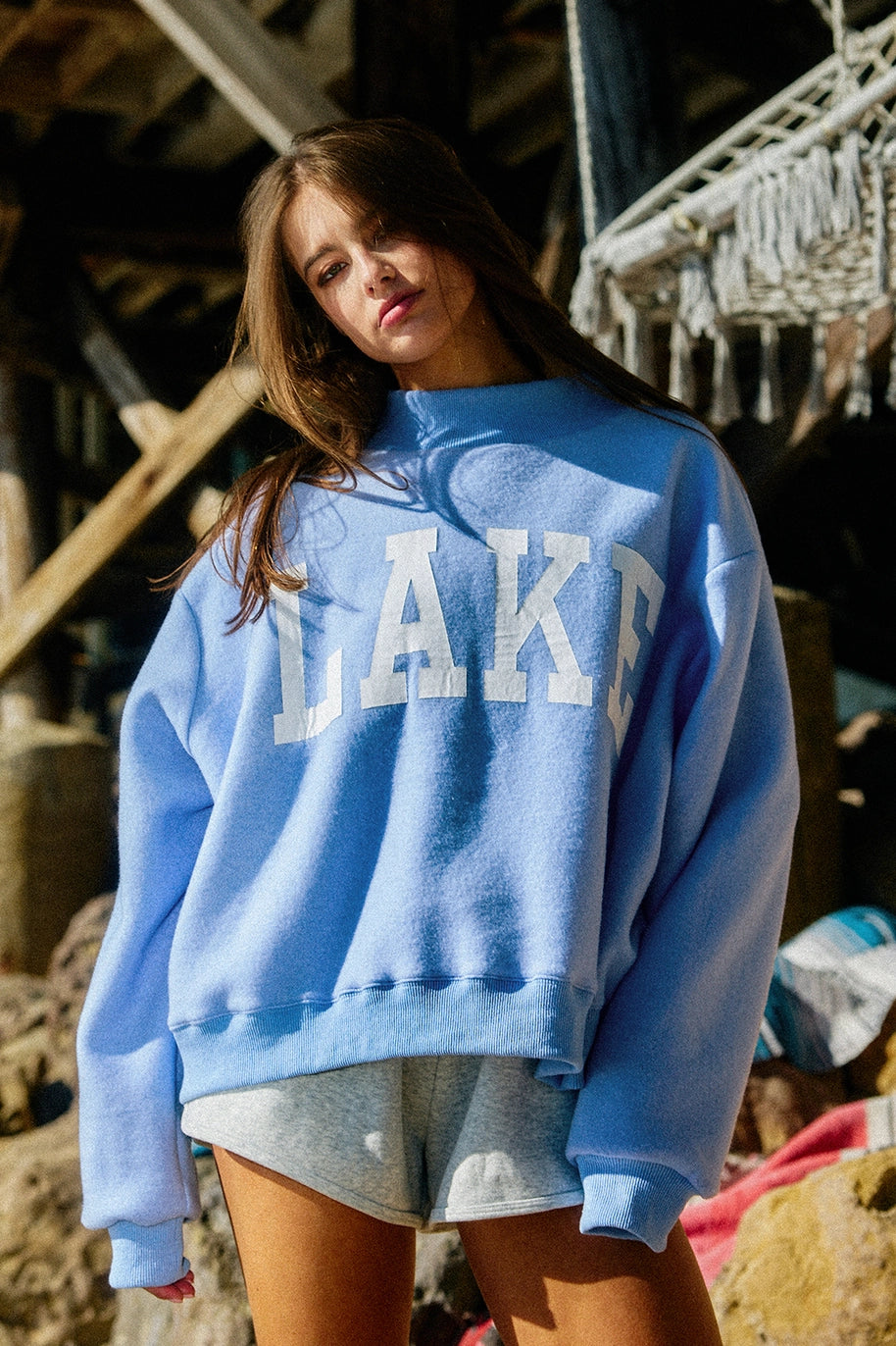 Woman wearing blue sweatshirt with 'LAKE' graphic outdoors