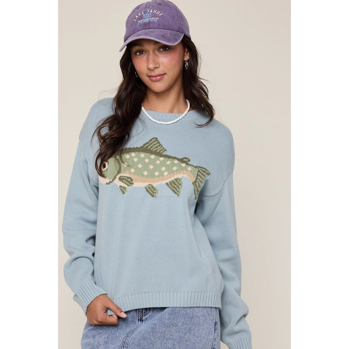 Woman wearing a light blue sweater with a fish design and a matching cap.