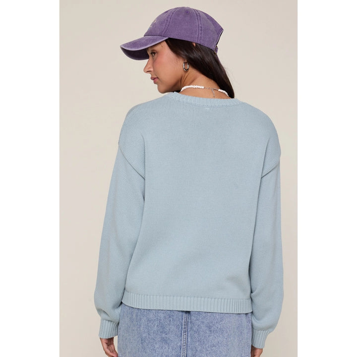 Person wearing a light blue sweater and purple cap on a beige background