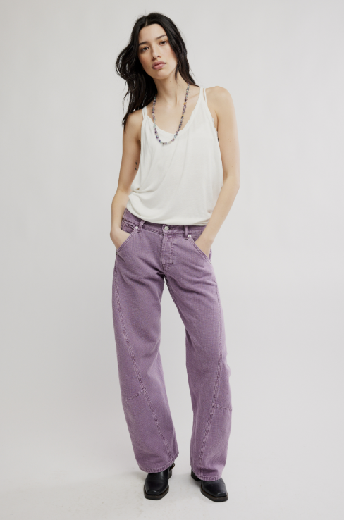 Woman wearing a white tank top and purple pants on a plain background