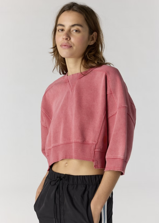 Woman wearing cropped red sweatshirt and black pants on plain background