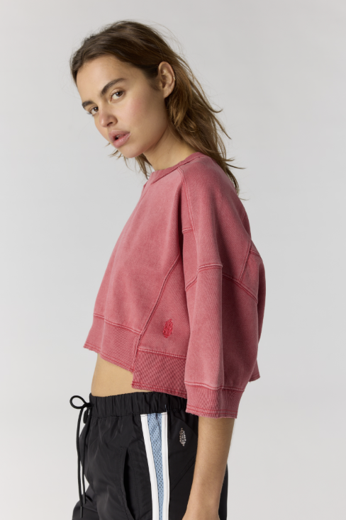 Woman wearing red cropped sweatshirt with black pants on plain background