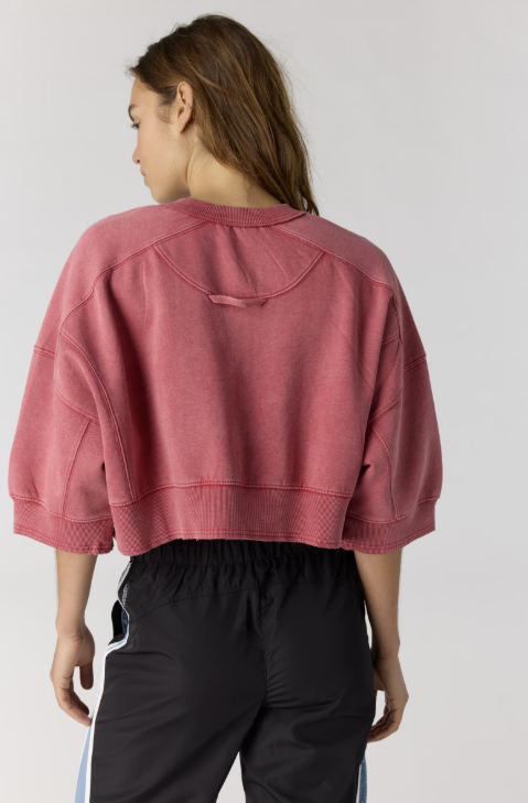 Woman shown from back wearing red cropped sweatshirt and black pants on plain background