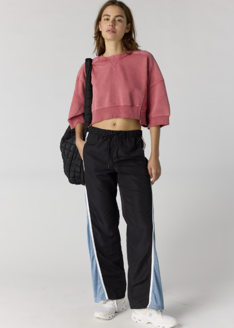 Woman wearing red cropped sweatshirt with black pants on plain background