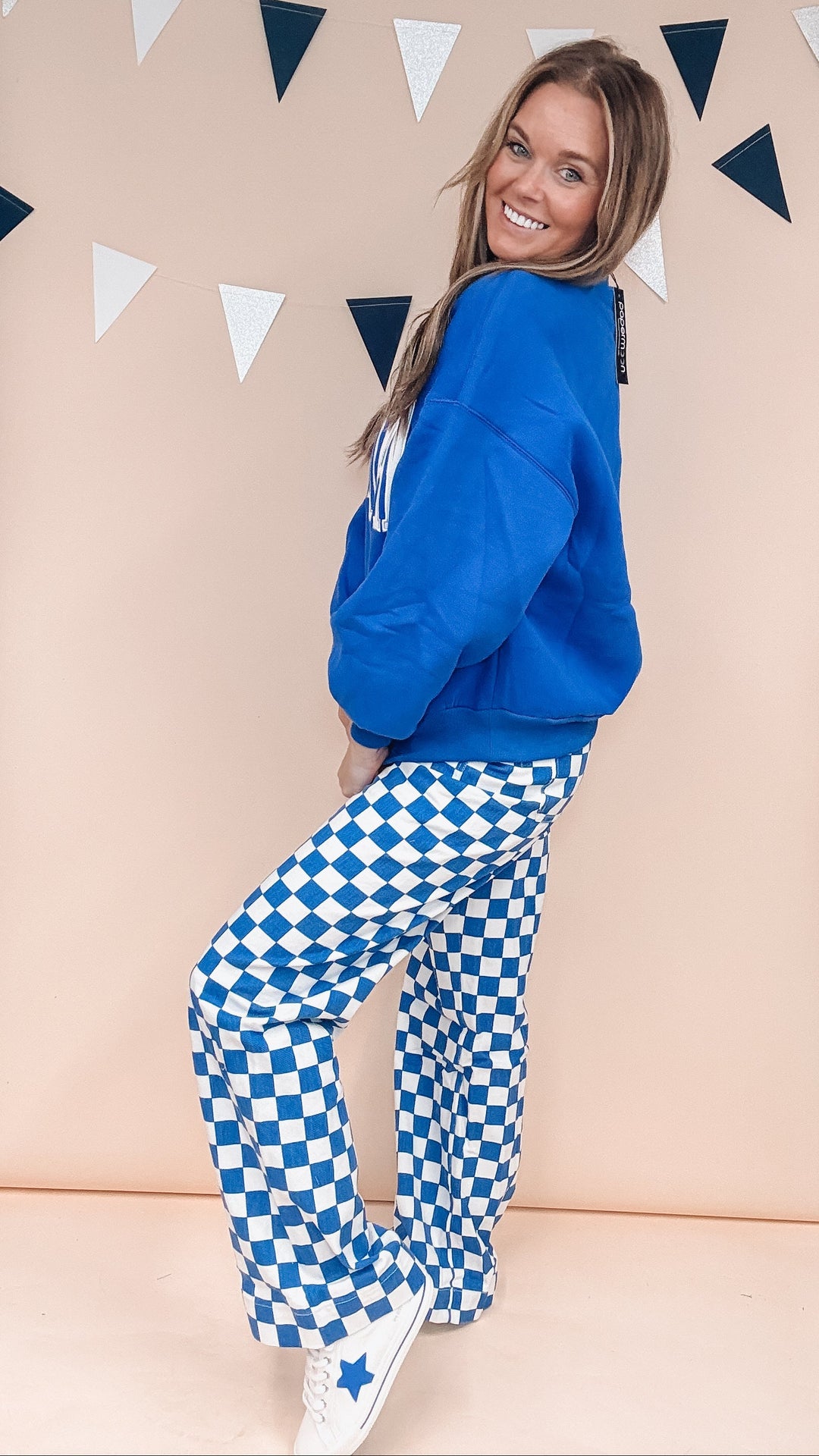 Woman wearing blue sweatshirt with blue and white checker pants on plain background