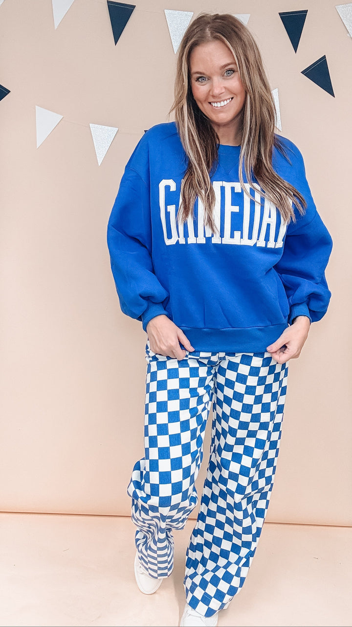Woman wearing blue gameday sweatshirt with blue and white checker pants on plain background