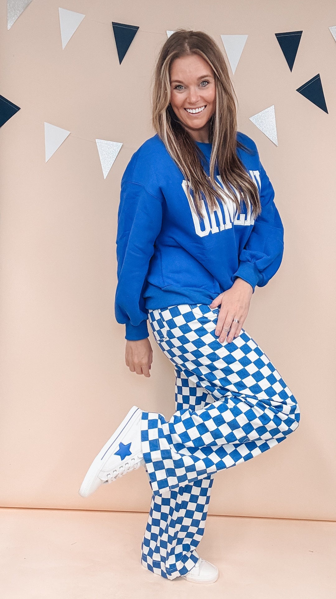 Woman wearing blue gameday sweatshirt with blue and white checker pants on plain background