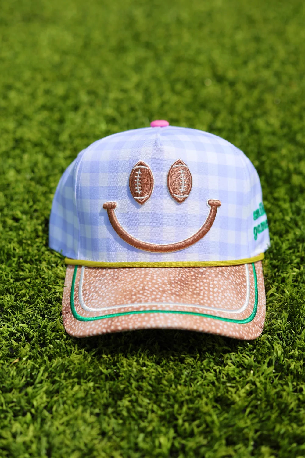 Blue gingham trucker hat with football smiley face and fawn print bill sitting on grass