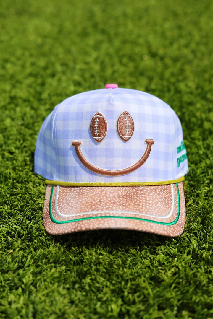 Blue gingham trucker hat with football smiley face and fawn print bill sitting on grass