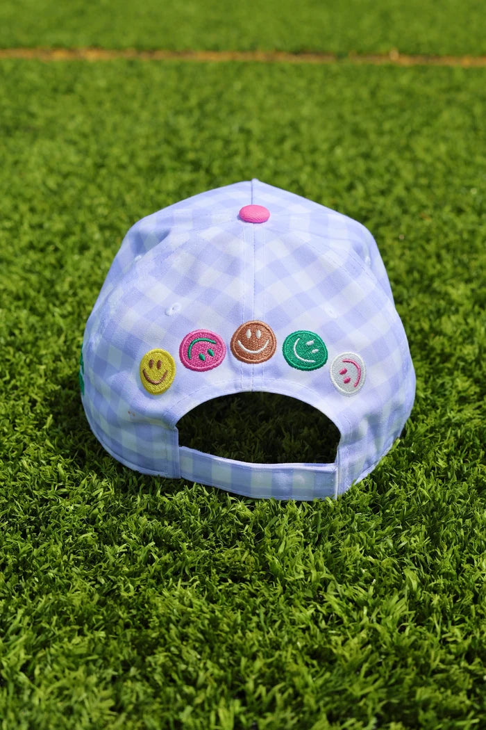 Blue gingham trucker hat with smiley faces across back sitting on grass