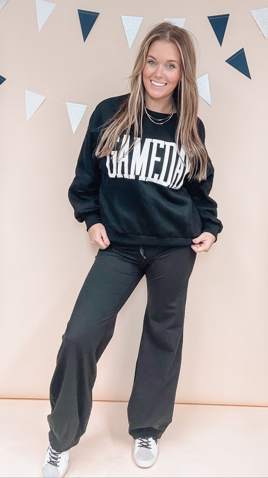 Woman wearing black sweatshirt with 'GAMEDAY' across front with black pants on plain background