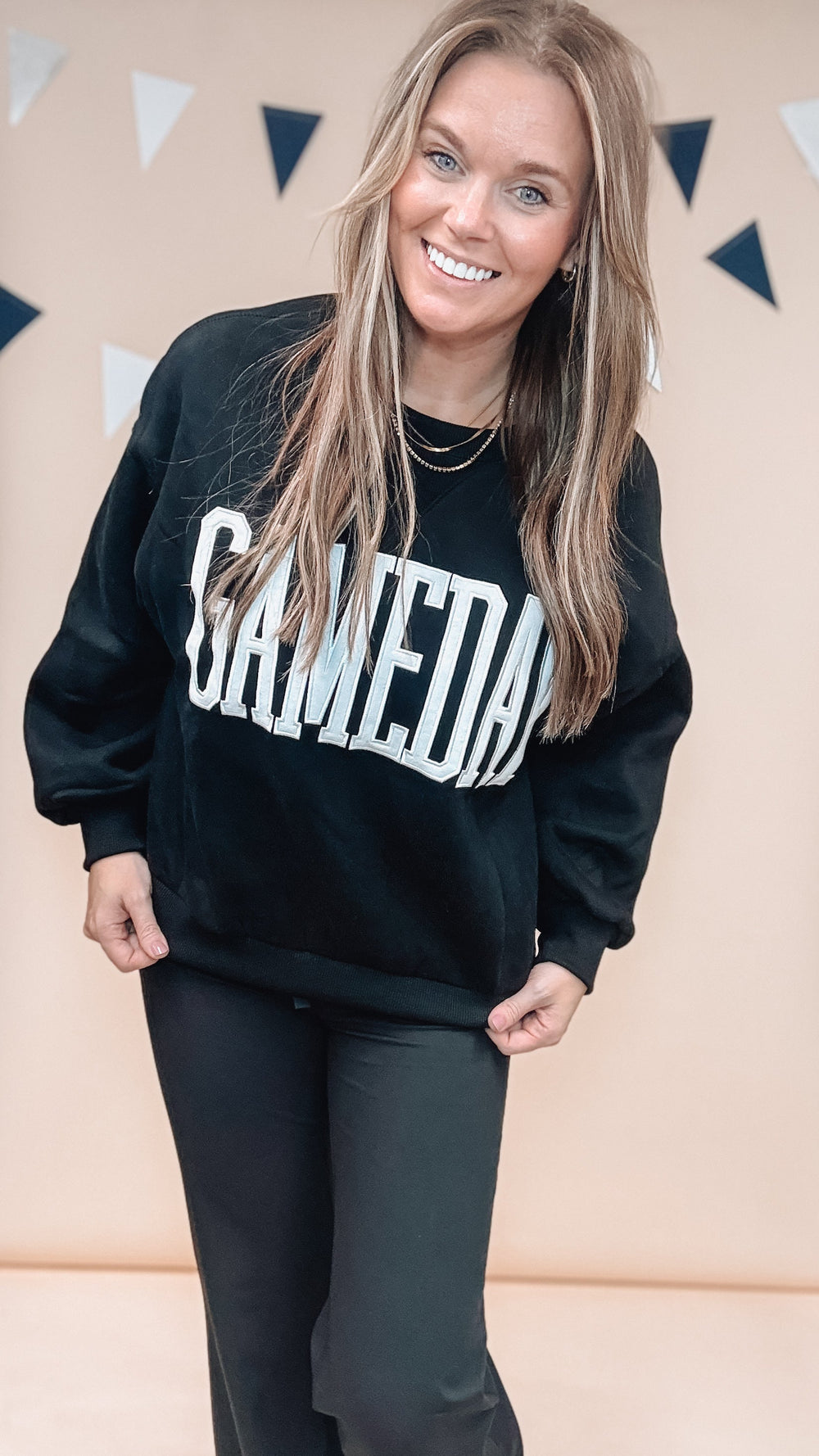 Woman wearing black sweatshirt with 'GAMEDAY' across front with black pants on plain background