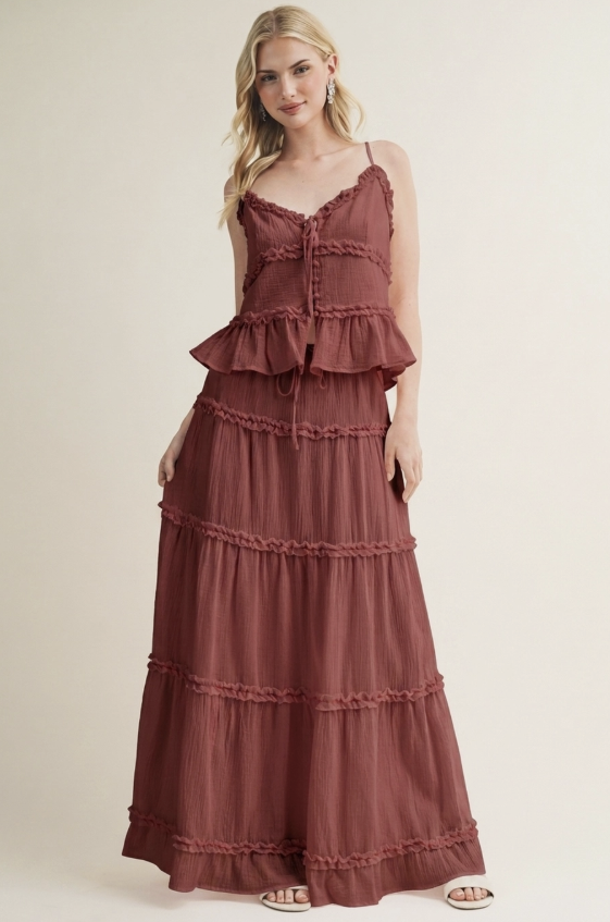 A woman modeling a rust-brown tiered maxi dress with ruffle trim and spaghetti straps against a plain beige studio background.