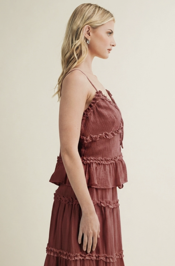 A woman in profile wearing a dusty rose tiered ruffle dress against a solid light beige background.