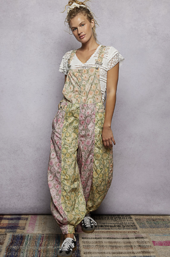 Woman wearing yellow and pink floral overalls with white tee on plain background