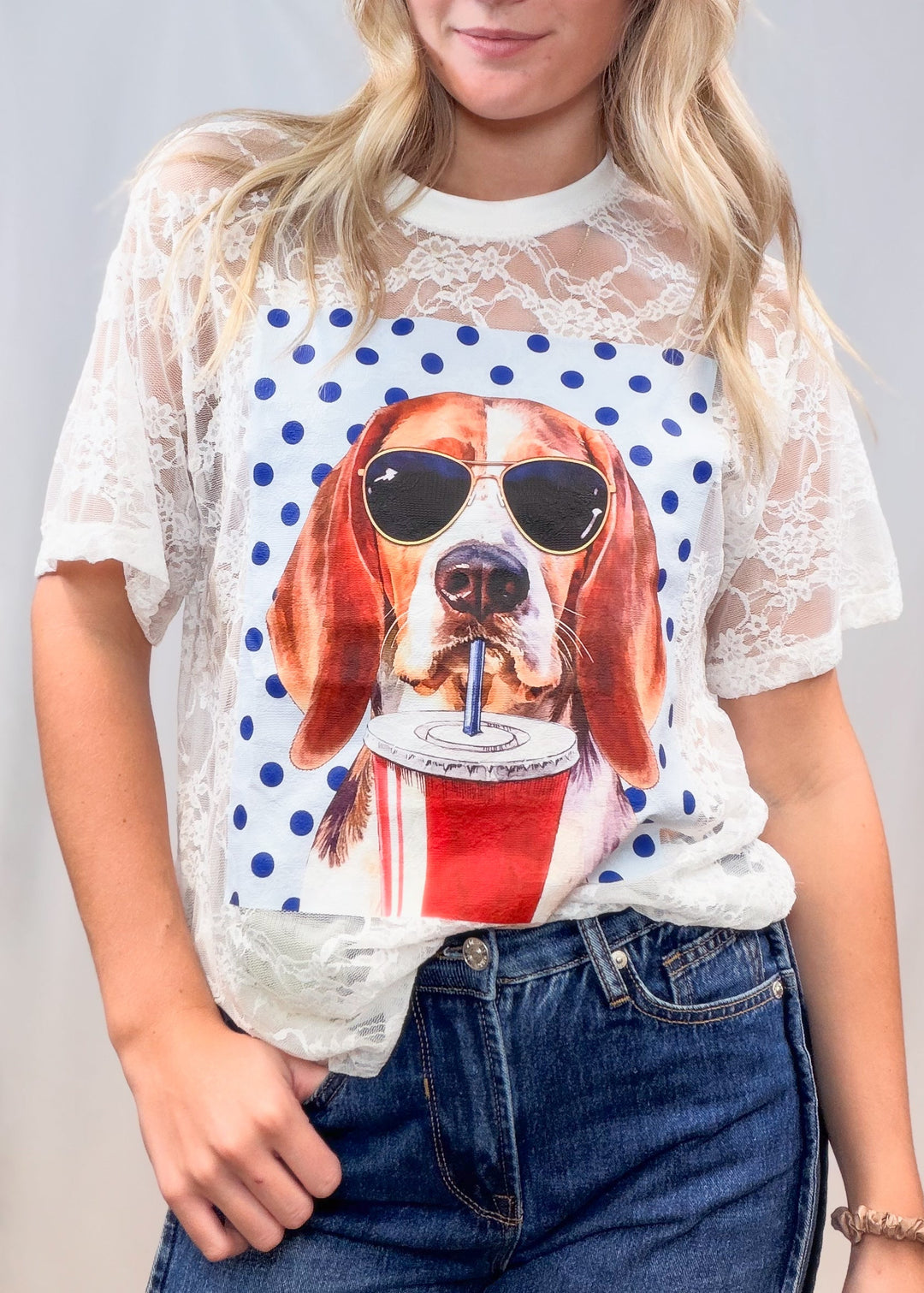 Woman wearing white lace tee with beagle graphic on front with denim jeans on plain background