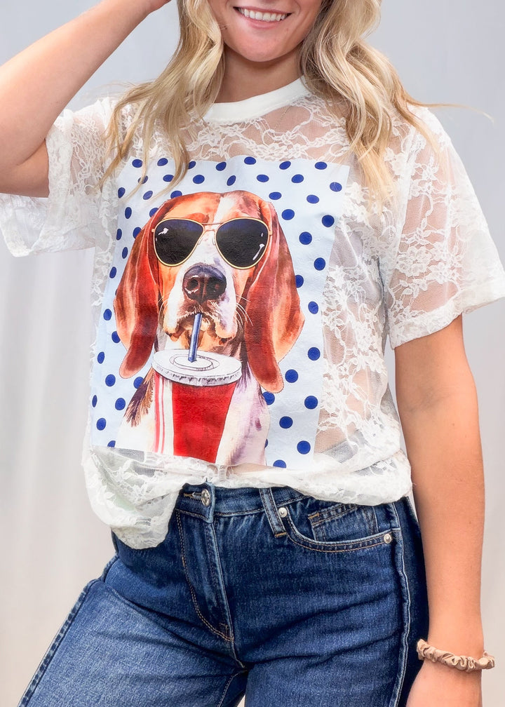 Woman wearing white lace tee with beagle graphic on front and denim jeans on plain background