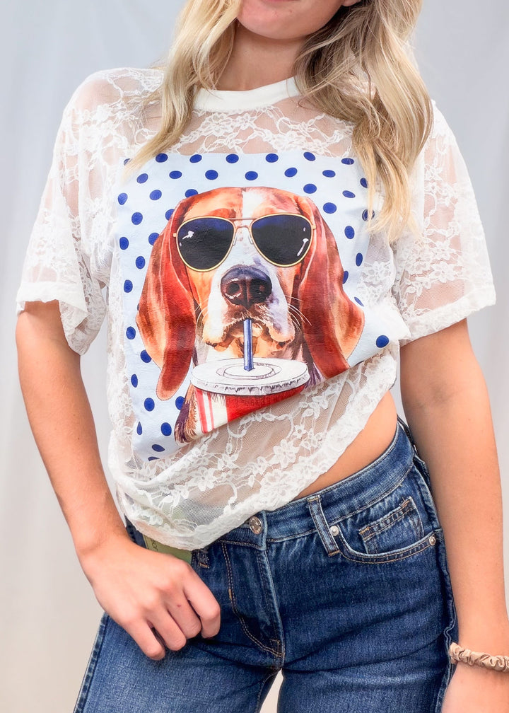 Woman wearing white lace tee with beagle graphic on front and denim jeans on plain background