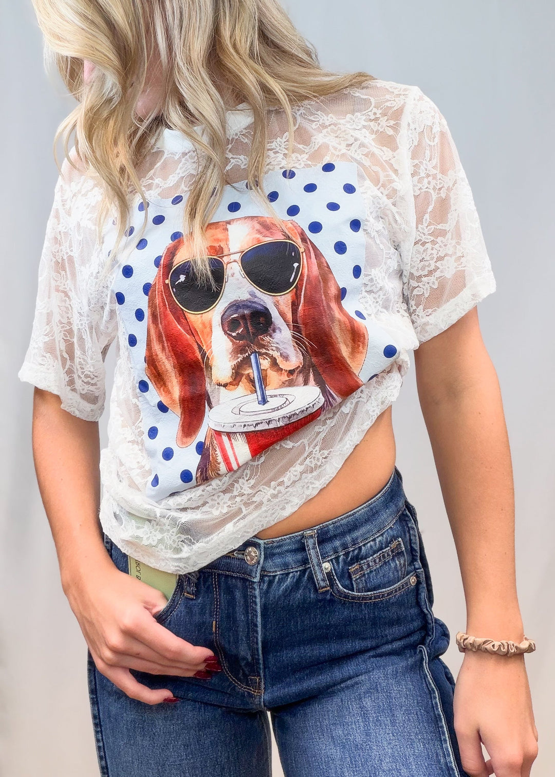 Woman wearing white lace tee with beagle graphic on front with denim jeans on plain background
