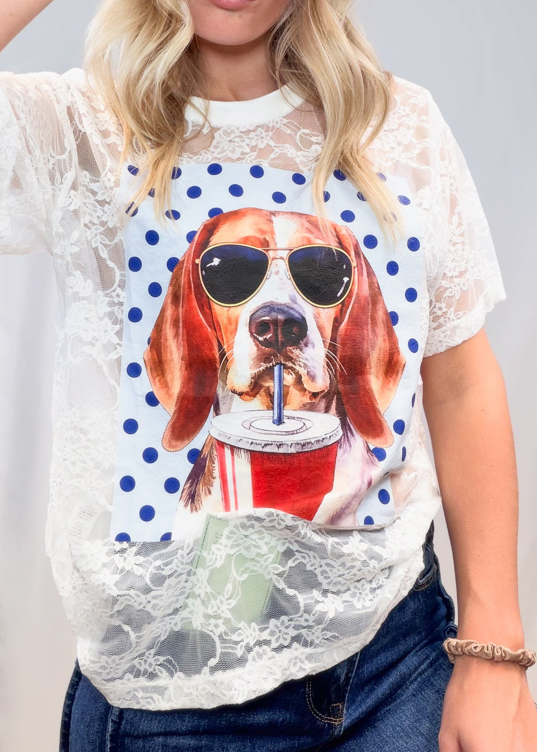 Woman wearing white lace tee with beagle graphic on front with denim jeans on plain background