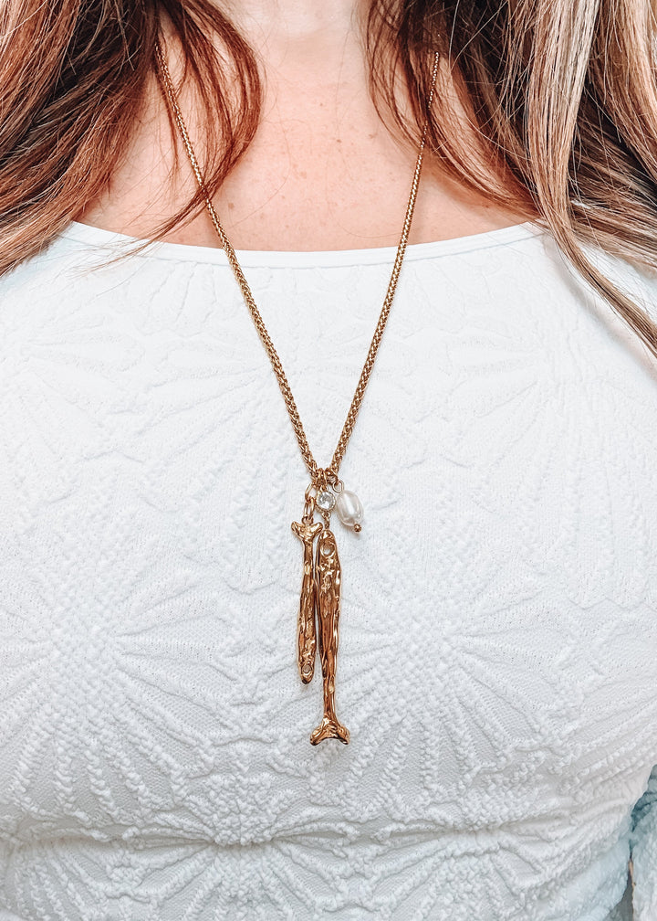Woman wearing white shirt with gold fish pendant and pearl 