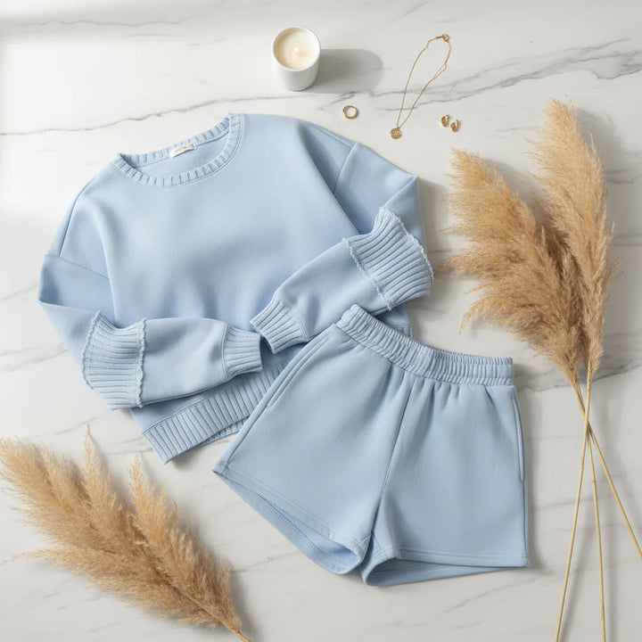 Light blue sweater and shorts set on a marble surface with pampas grass and a candle.