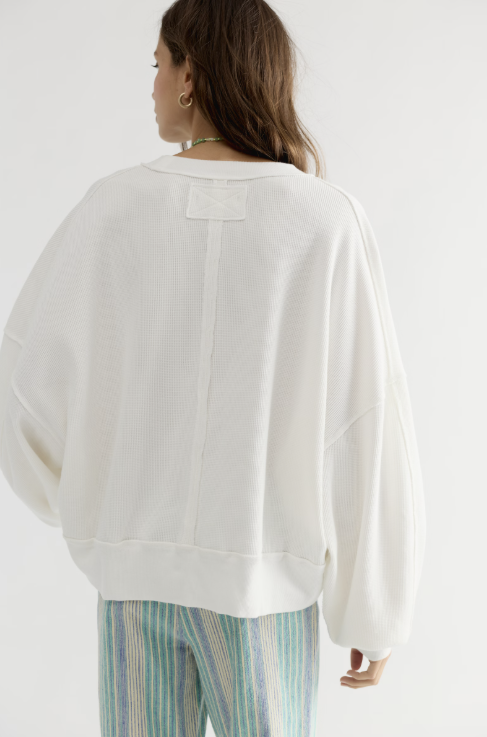 A woman shown from the back wearing a loose white long-sleeve sweatshirt and striped pants against a plain white studio background.