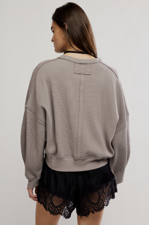 A woman shown from the back wearing a taupe-gray waffle-knit crewneck sweatshirt and black lace-trimmed shorts against a light gray studio background.