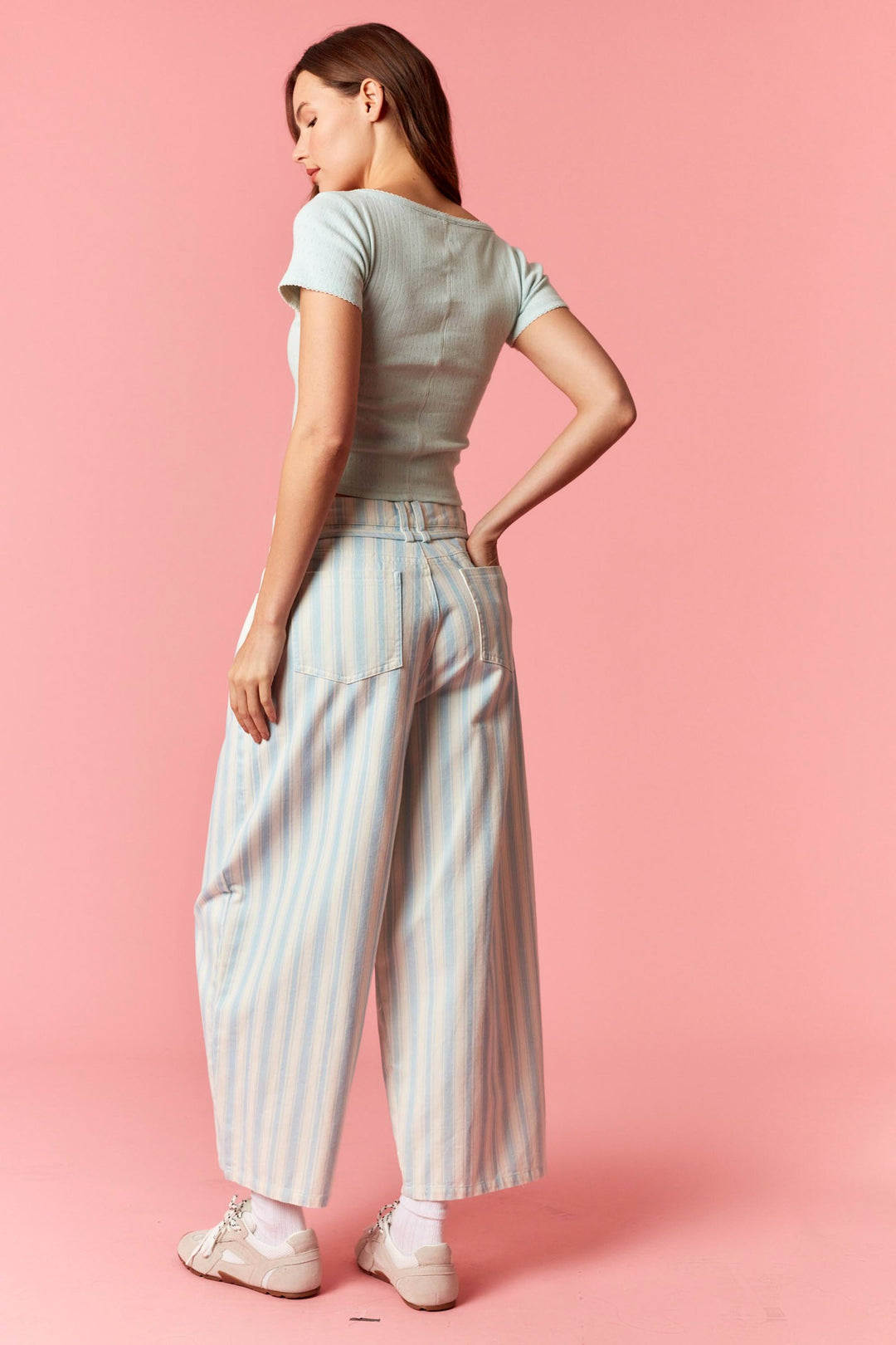 Back of woman wearing blue and white stripe pants and blue top on pink background