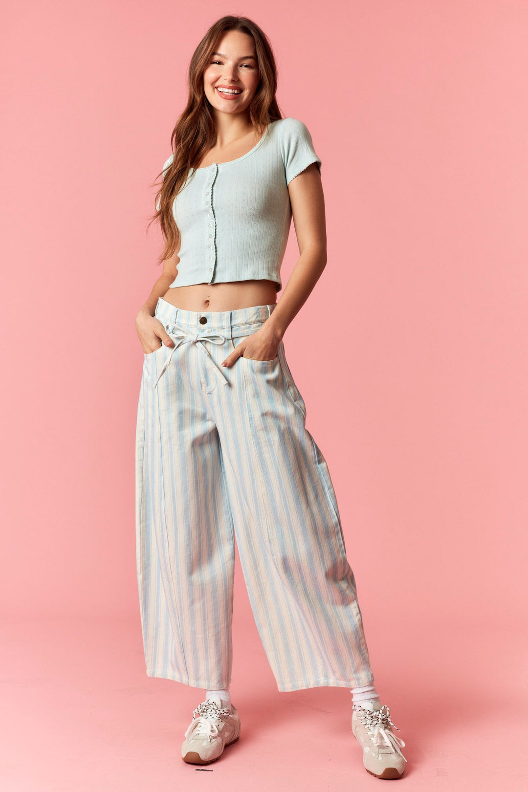 Woman wearing blue and white stripe pants and blue top on pink background