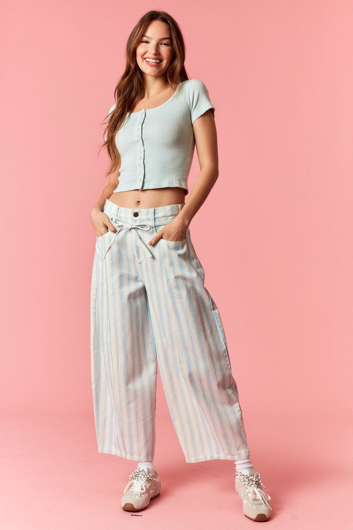 Woman wearing blue and white stripe pants and blue top on pink background