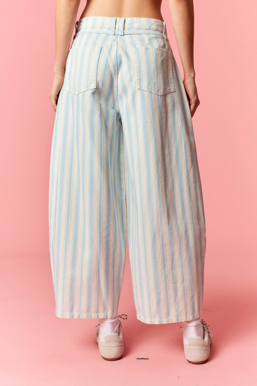 Back of person wearing blue and white stripe pants on pink background
