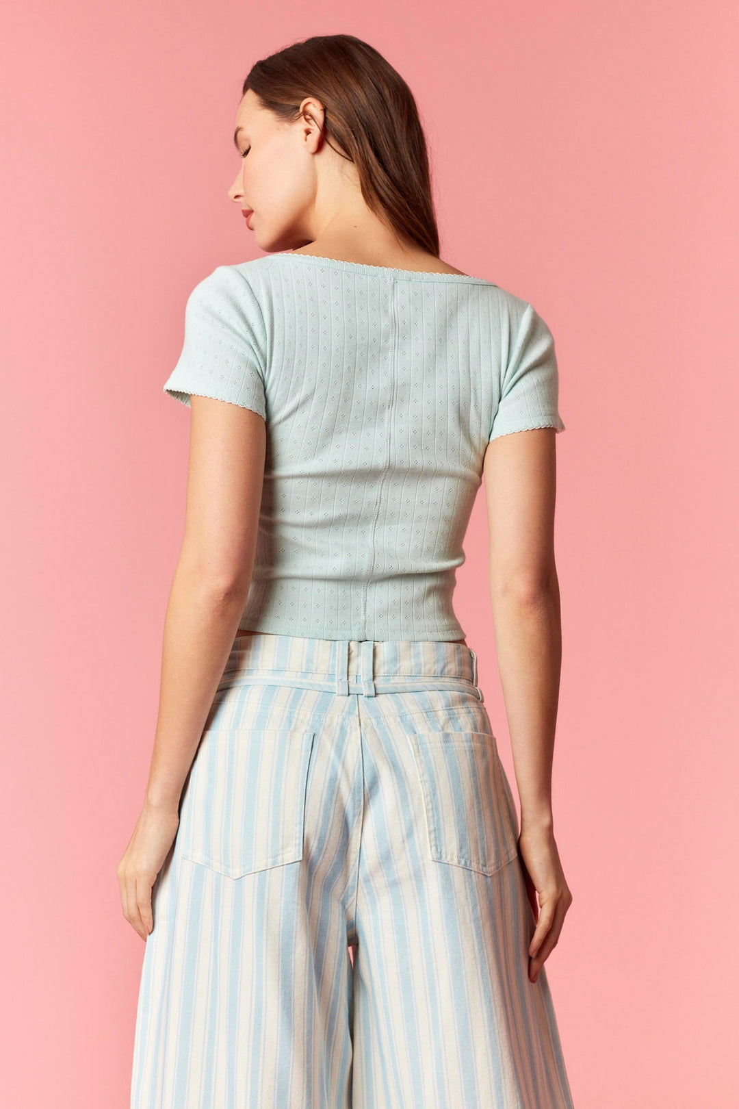Back of woman wearing blue and white stripe pants and blue top on pink background