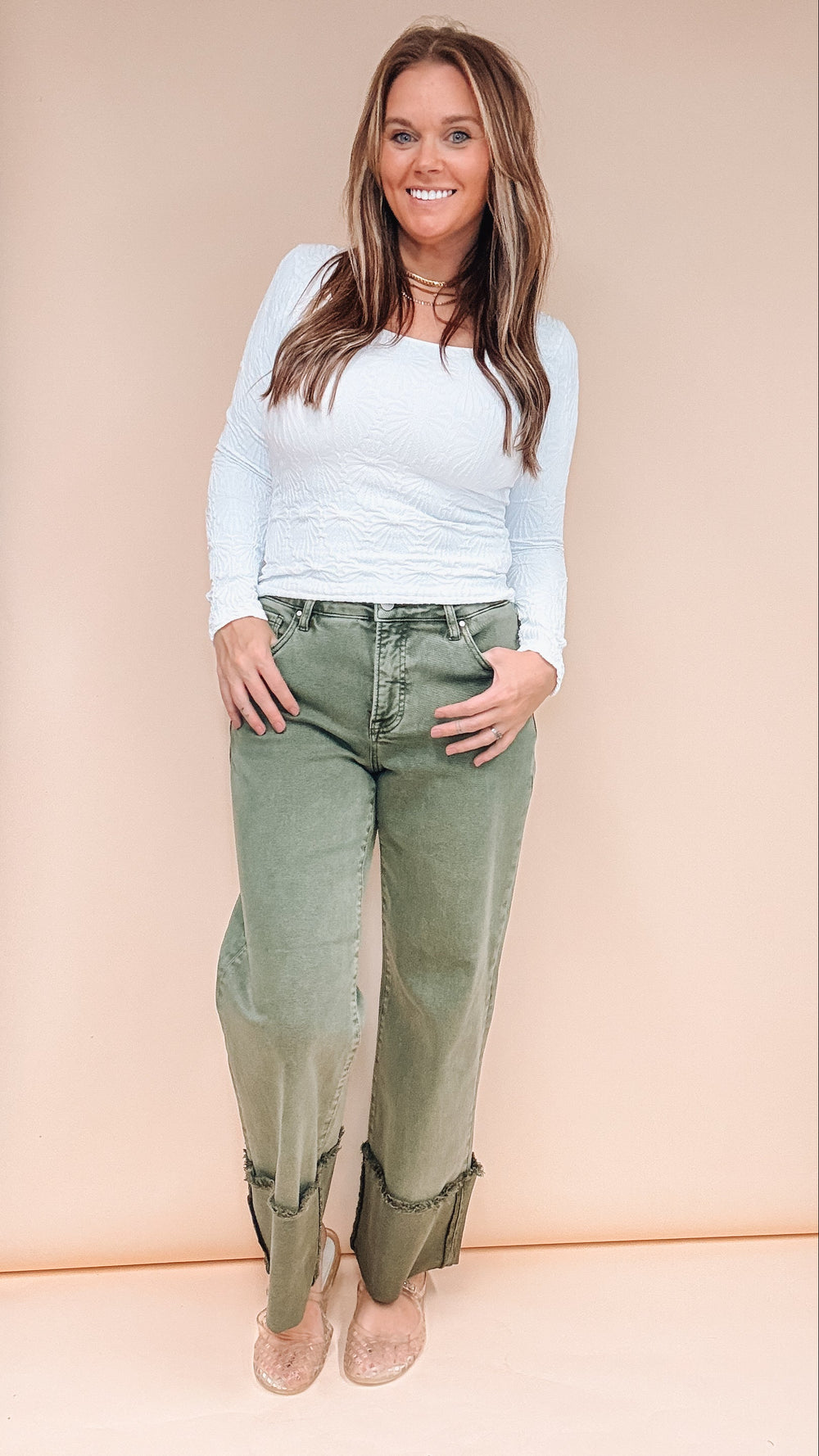 Woman wearing olive jeans and white long sleeve tee on plain background