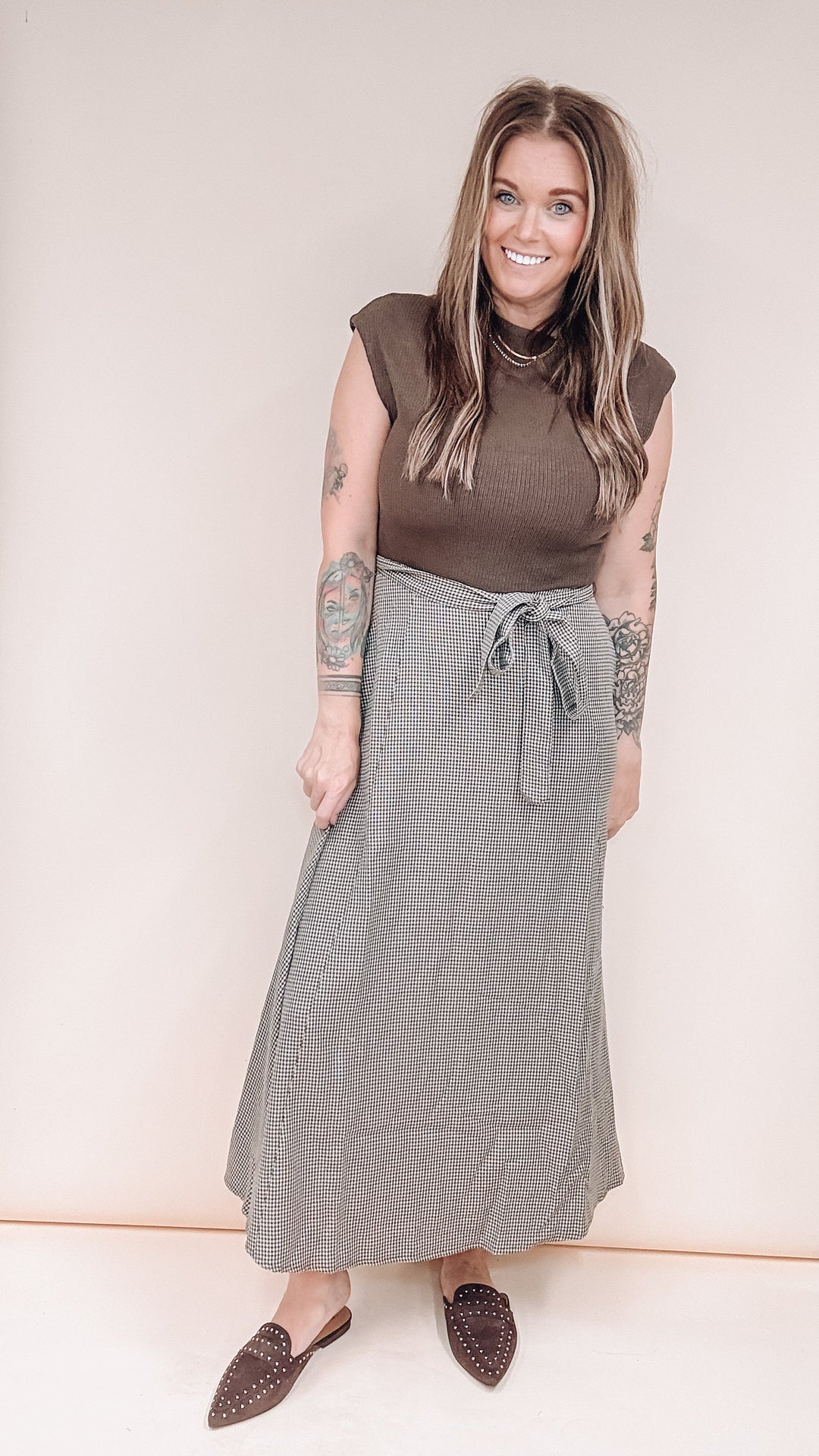 Woman wearing brown maxi dress with brown studded shoes on plain background