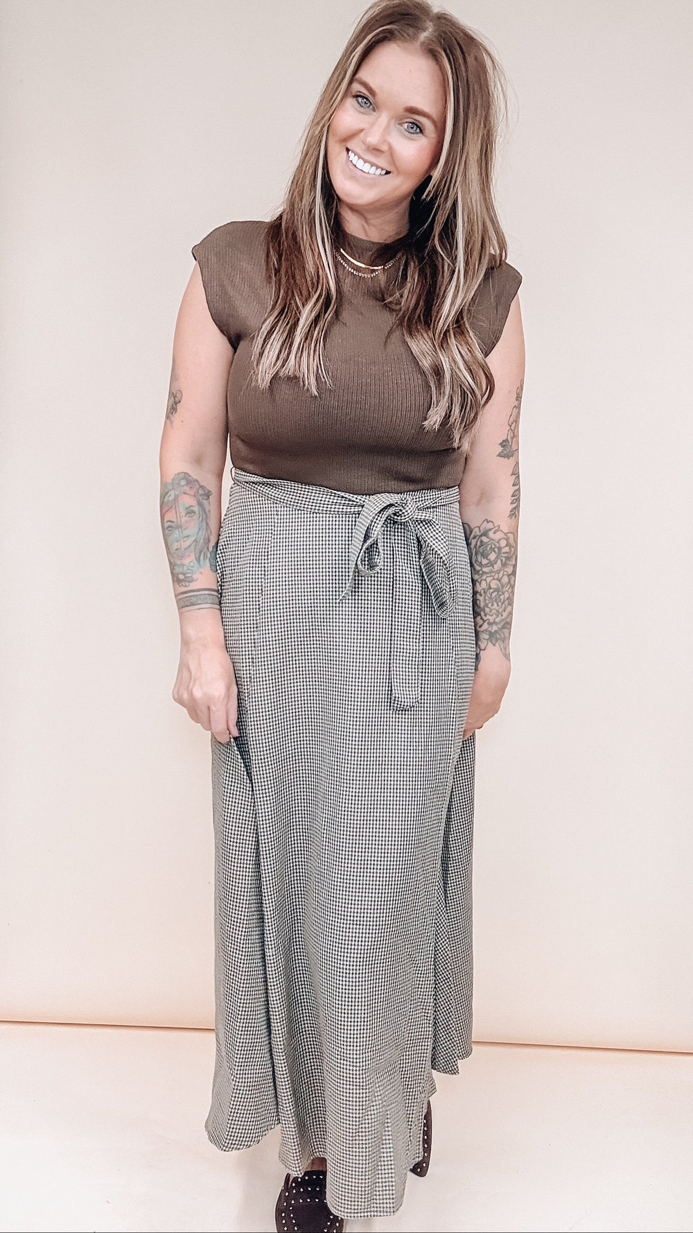 A woman modeling a brown short-sleeve knit top and a gray textured maxi skirt with a tie waist, standing against a plain beige studio background.