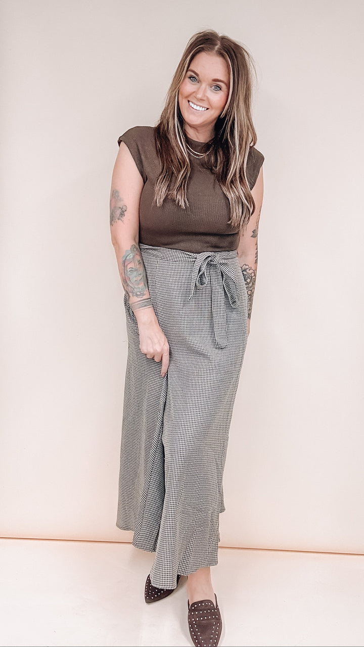 A woman modeling a brown sleeveless top and a high-waisted gray tie-waist maxi skirt, paired with brown studded loafers, against a plain beige studio background.