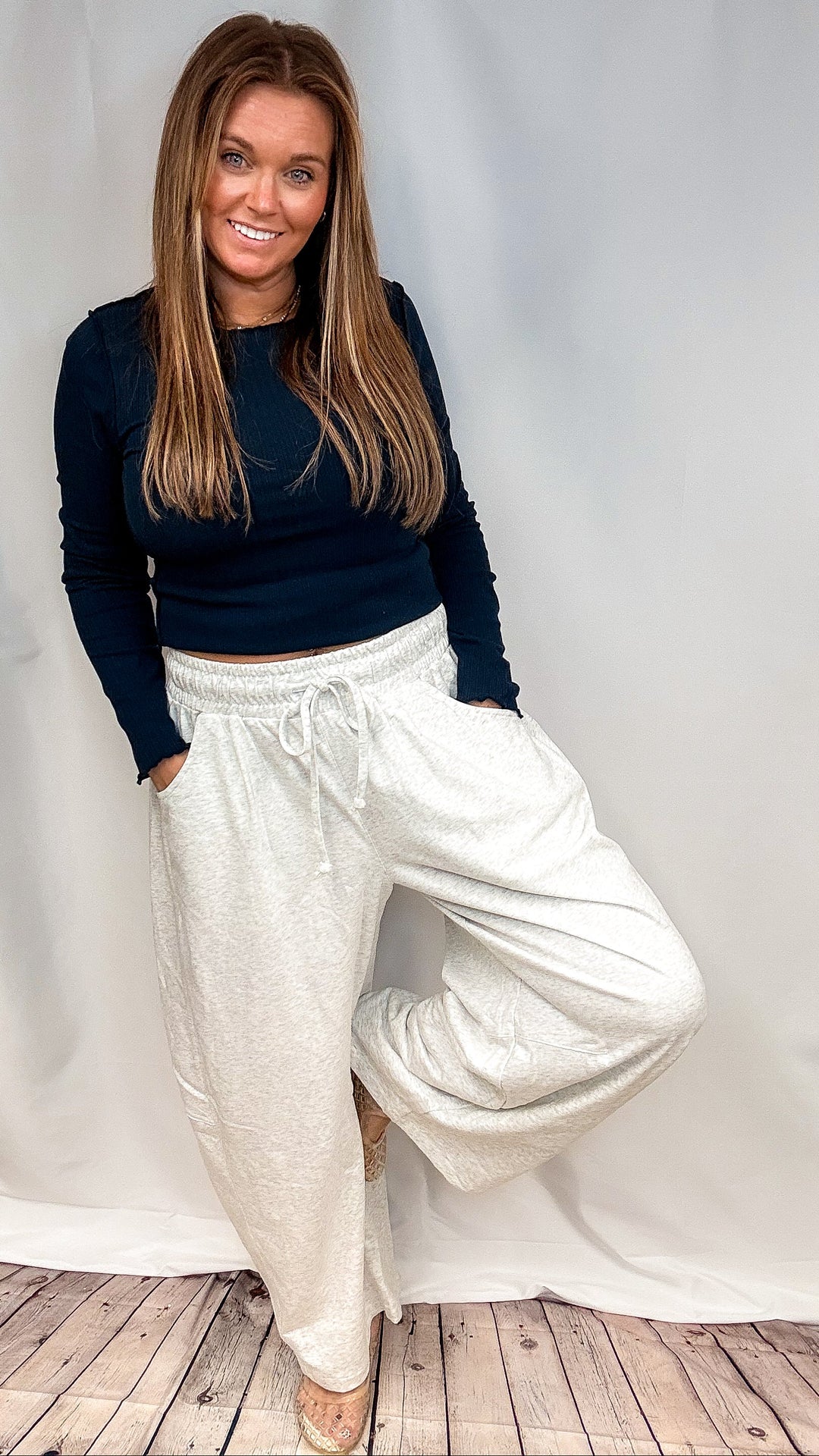 Woman wearing navy long sleeve shirt and grey sweatpants on plain background