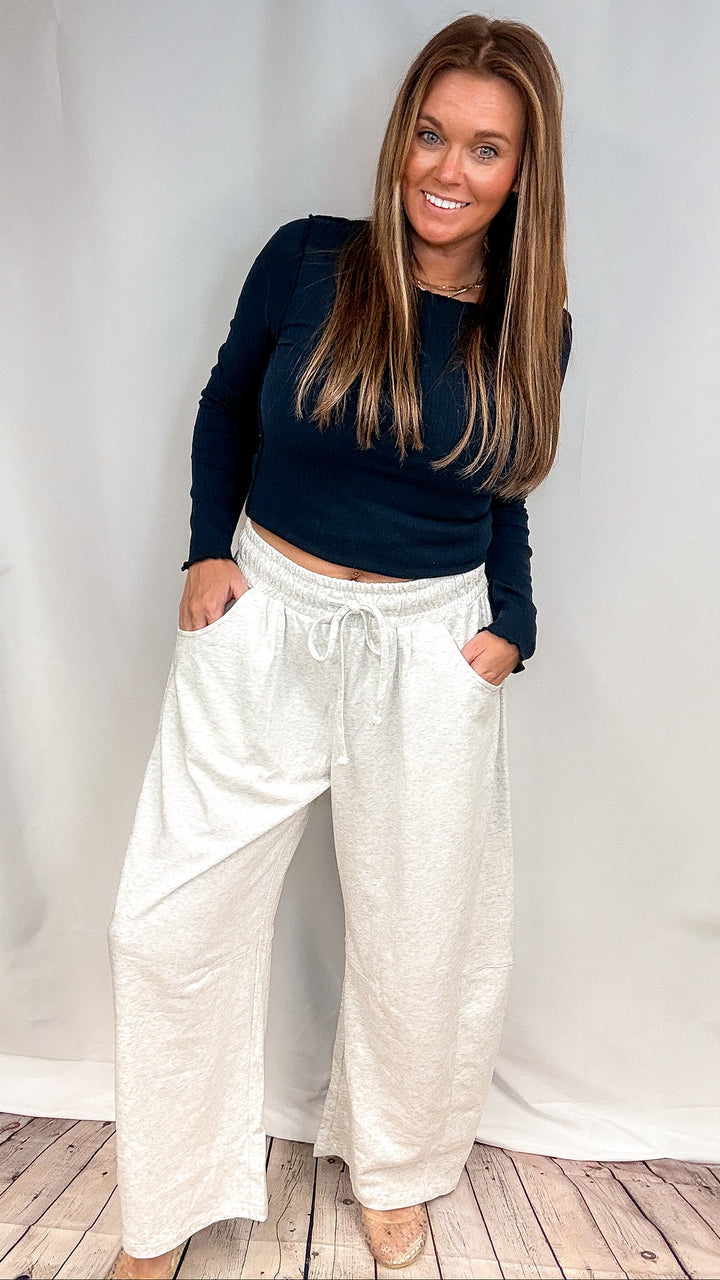 Woman wearing navy long sleeve top and grey sweatpants on plain background
