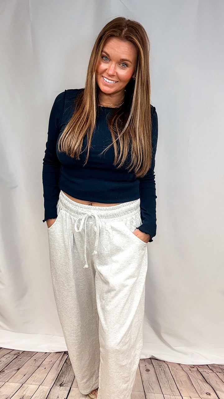A woman modeling a dark navy blue long-sleeve crop top and light beige heathered drawstring sweatpants against a white studio backdrop.
