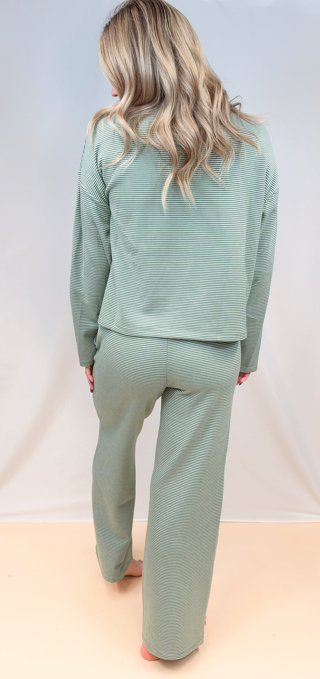 Woman shown from back view wearing green and cream pin stripe matching set on plain background