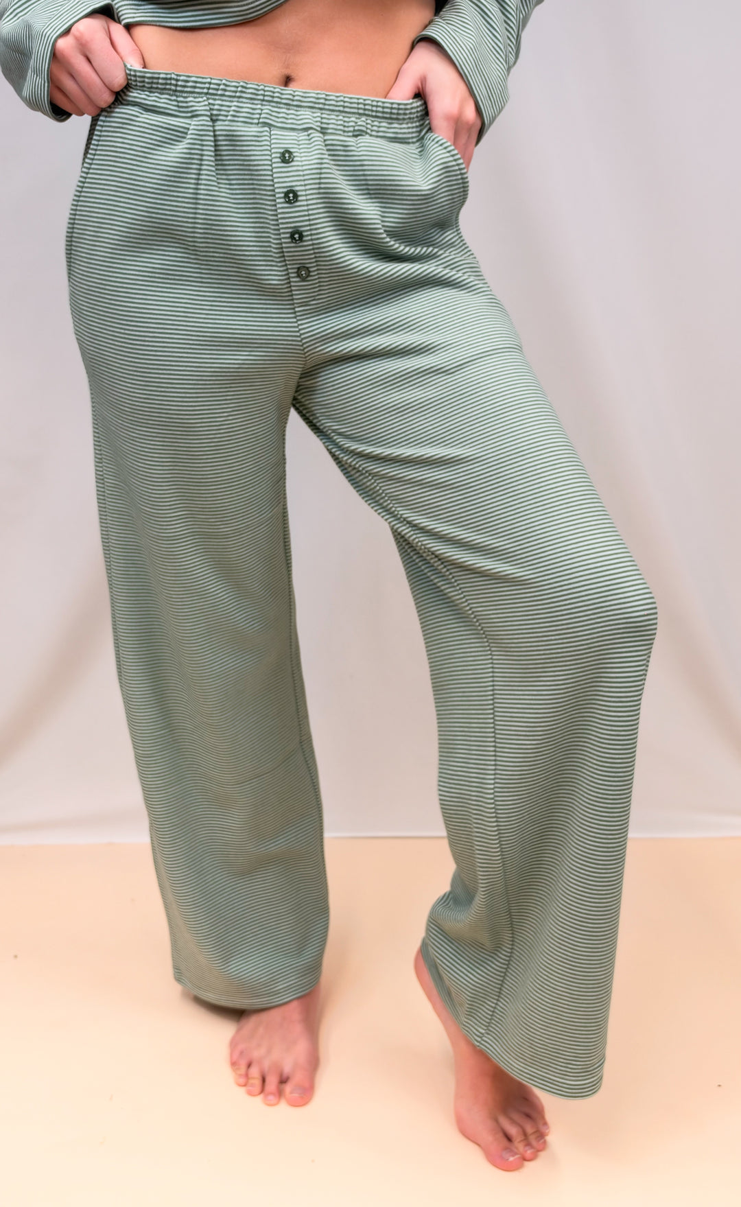 Woman shown from waist down wearing green and cream pinstripe pants on plain background