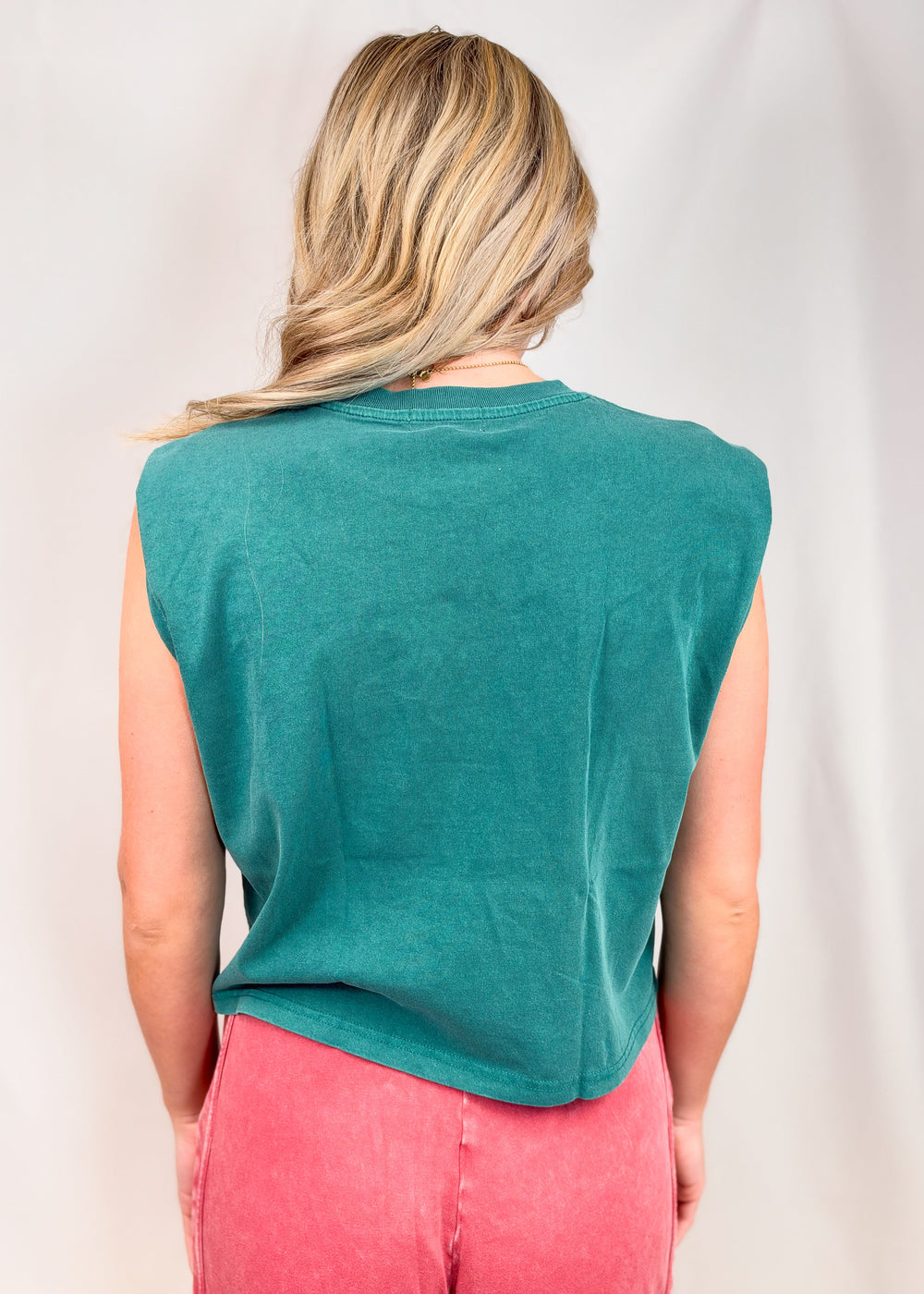 Woman shown from back wearing teal muscle tee and red pants on plain background